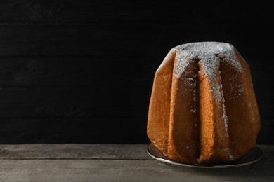 Photo of Delicious Pandoro cake decorated with powdered sugar on wooden table against black background, space for text. Traditional Italian pastry