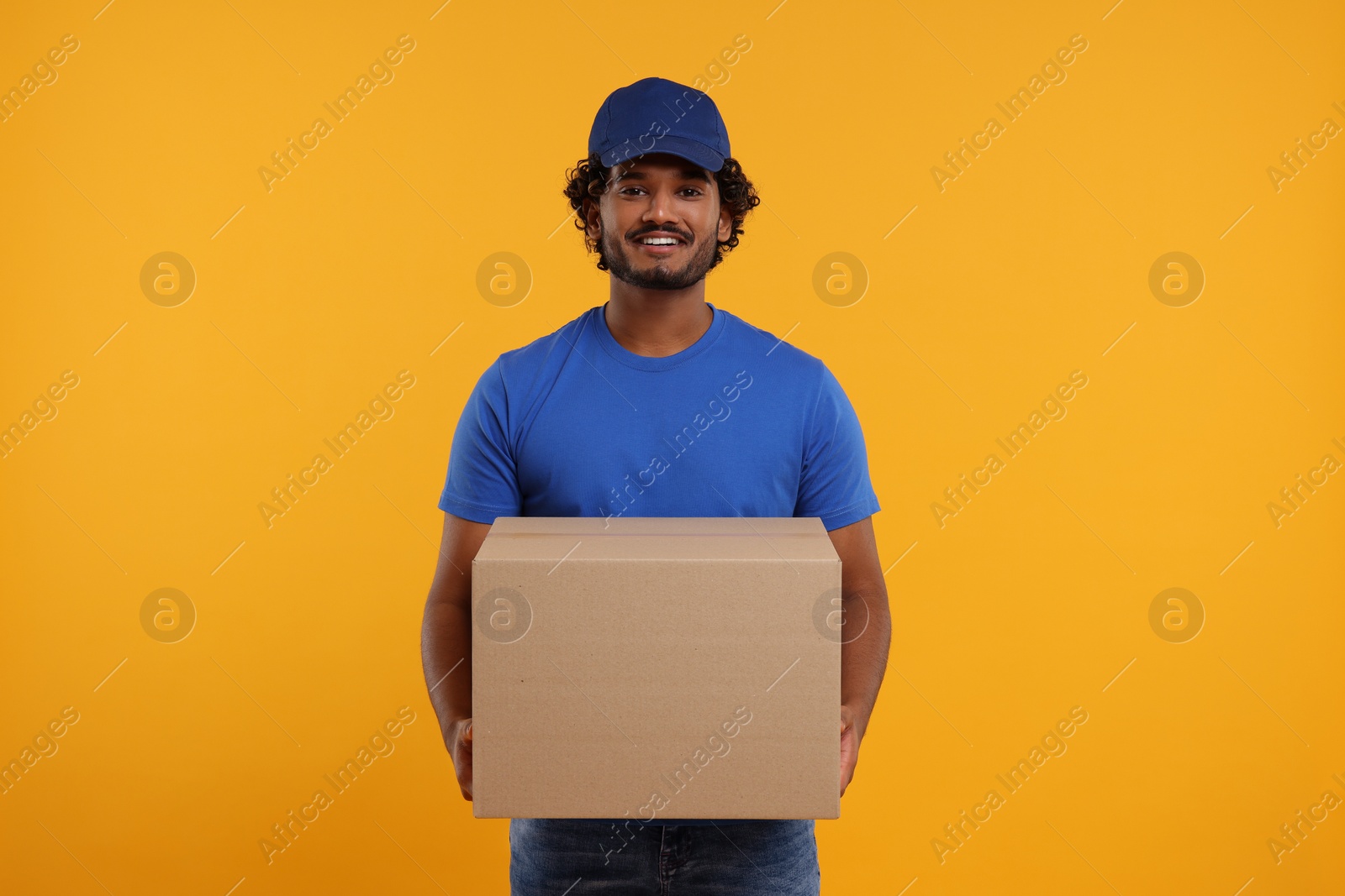 Photo of Happy young courier with parcel on orange background