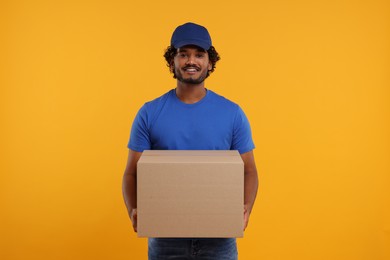 Photo of Happy young courier with parcel on orange background