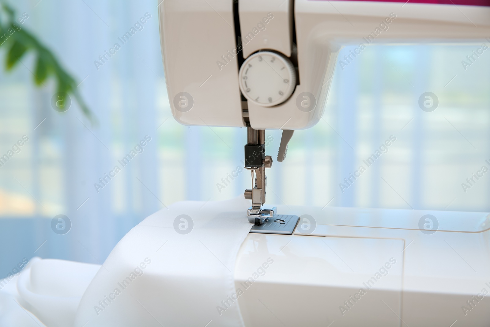 Photo of Sewing machine with textile near window, closeup