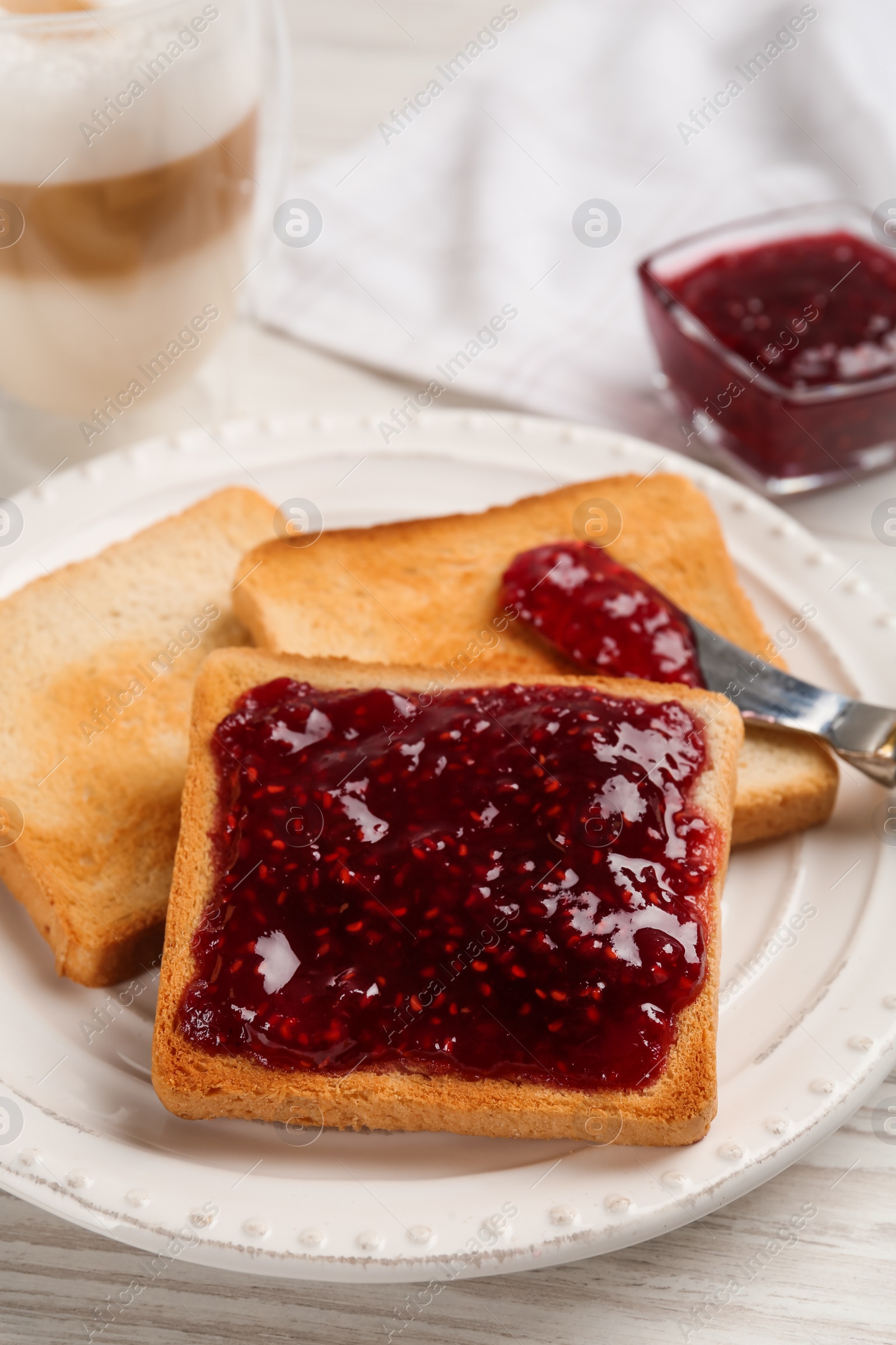 Photo of Toast with tasty raspberry jam and roasted slices of bread on white wooden table, closeup