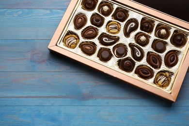 Box of delicious chocolate candies on light blue wooden table, top view. Space for text