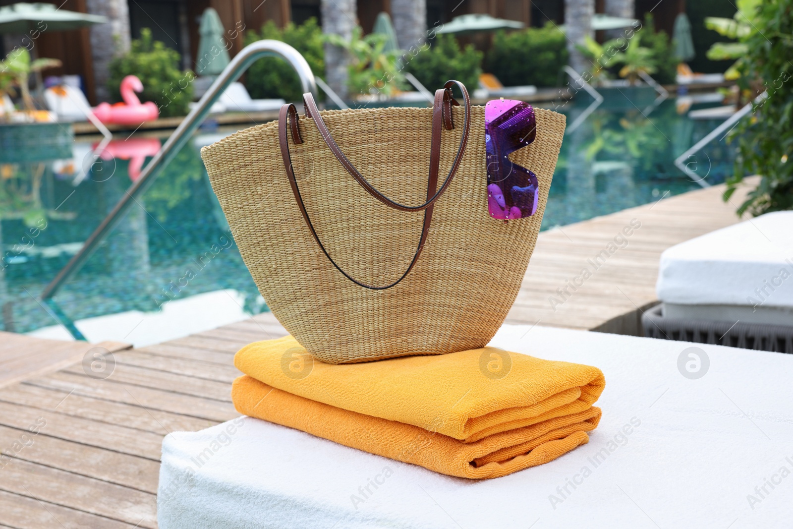 Photo of Wicker bag with beach accessories on sunbed near outdoor swimming pool. Luxury resort