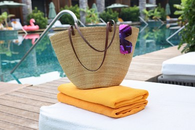 Photo of Wicker bag with beach accessories on sunbed near outdoor swimming pool. Luxury resort