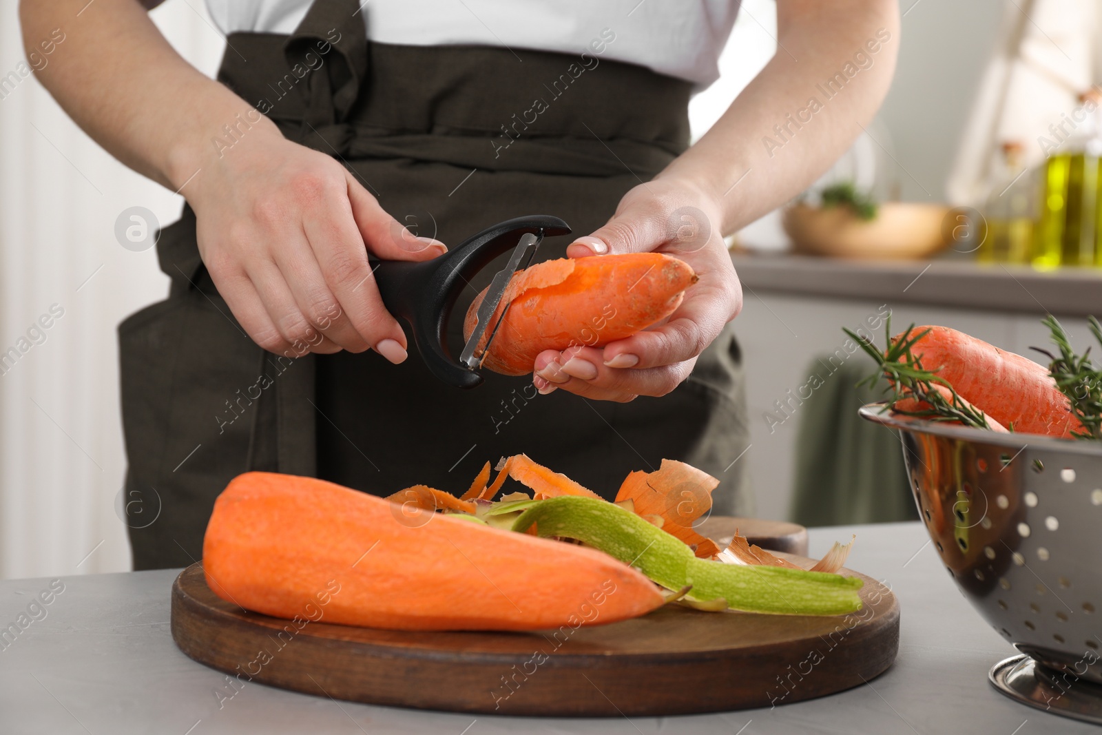 Photo of Woman peeling fresh carrot at light table indoors, closeup