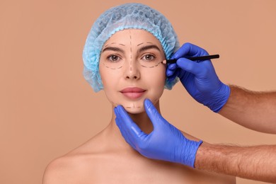 Doctor drawing marks on woman's face for cosmetic surgery operation against beige background