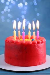 Cute bento cake with tasty cream and burning candles on light blue wooden table