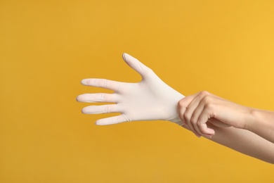 Photo of Doctor wearing medical gloves on yellow background, closeup