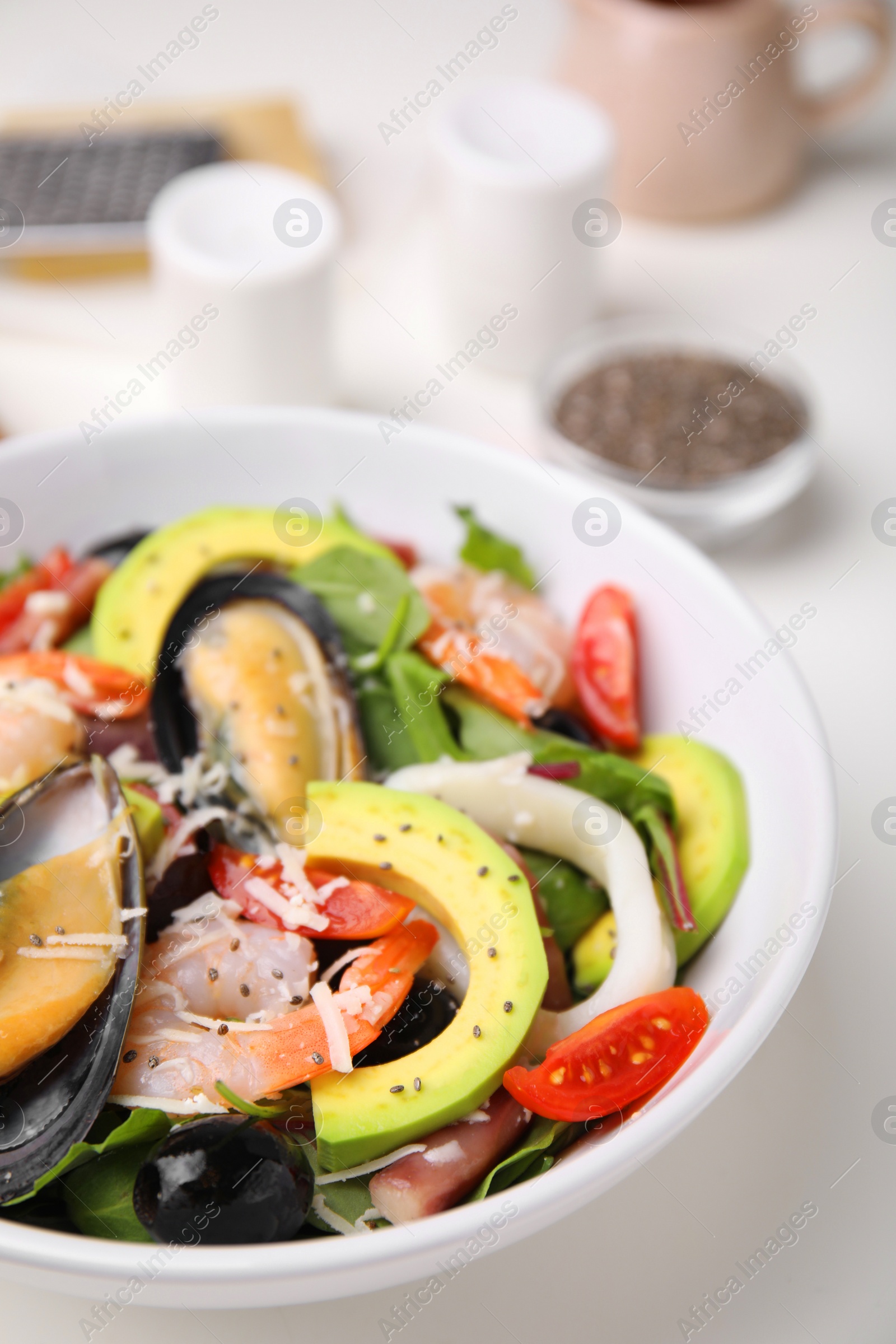 Photo of Bowl of delicious salad with seafood on white table, closeup