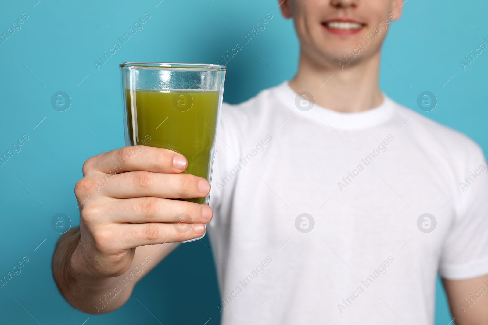 Photo of Young man with glass of juice on light blue background, closeup