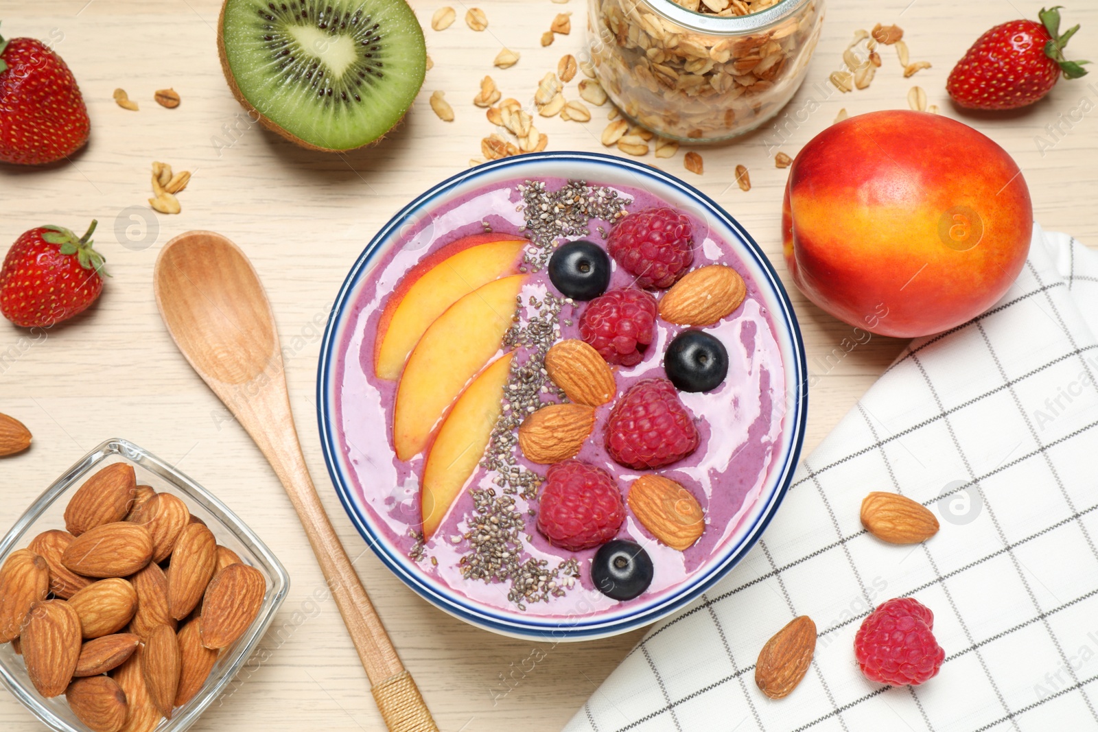 Photo of Delicious acai smoothie with fruits and almonds served on wooden table, flat lay