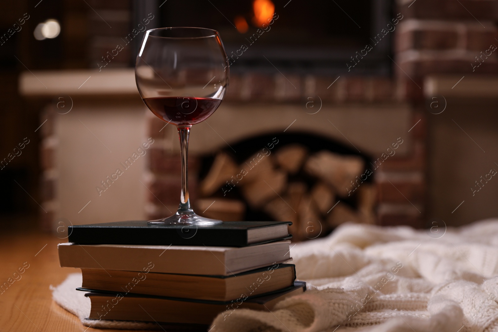Photo of Glass of wine on books near fireplace indoors. Space for text