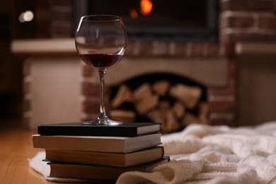 Glass of wine on books near fireplace indoors. Space for text