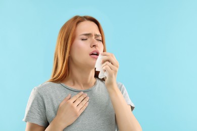 Photo of Suffering from allergy. Young woman with tissue sneezing on light blue background, space for text
