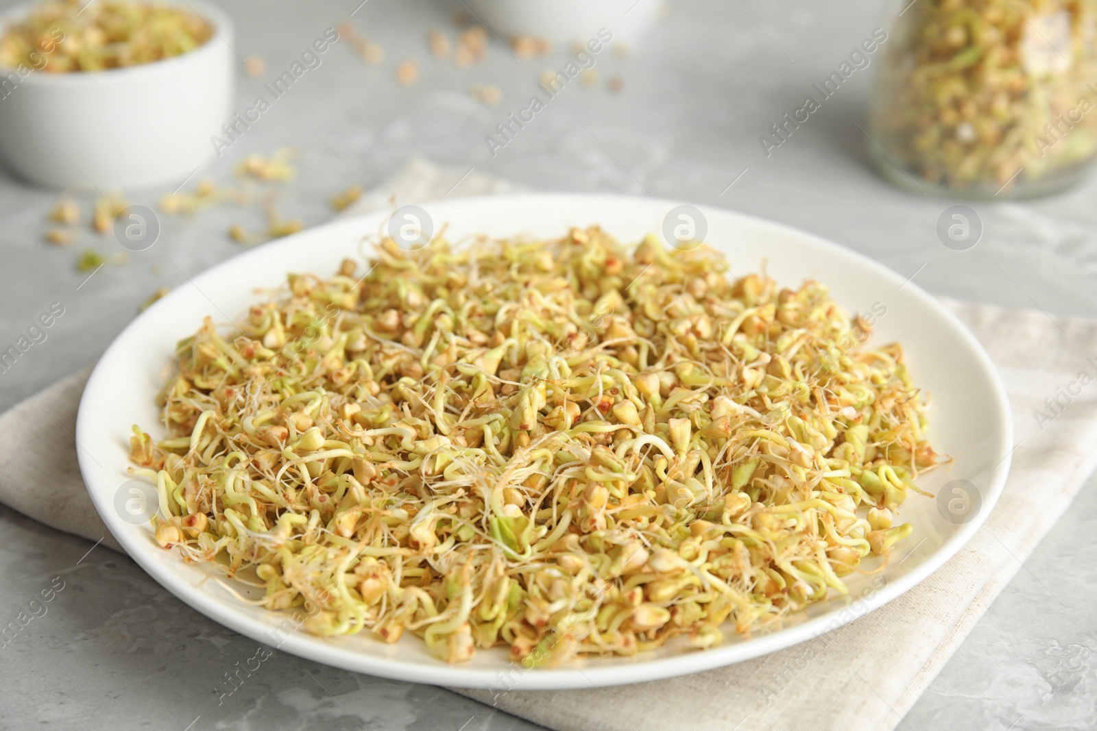 Photo of Plate of sprouted green buckwheat on light grey table, closeup