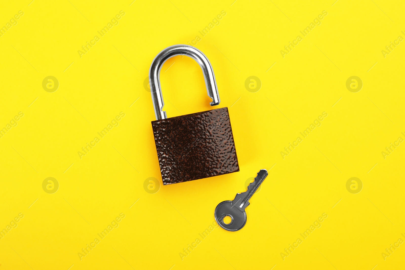 Photo of Modern padlock with key on yellow background, flat lay