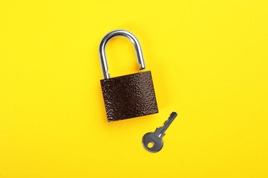 Photo of Modern padlock with key on yellow background, flat lay