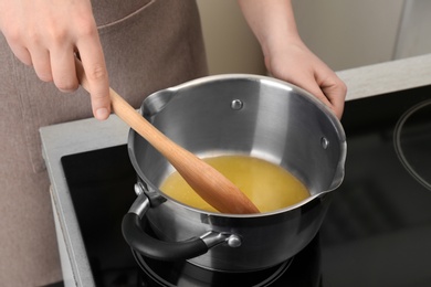 Photo of Woman stirring butter in saucepan on electric stove, closeup