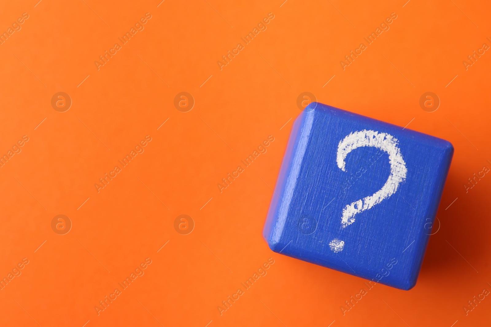 Photo of Blue wooden cube with question mark on orange background, top view. Space for text
