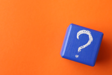Photo of Blue wooden cube with question mark on orange background, top view. Space for text