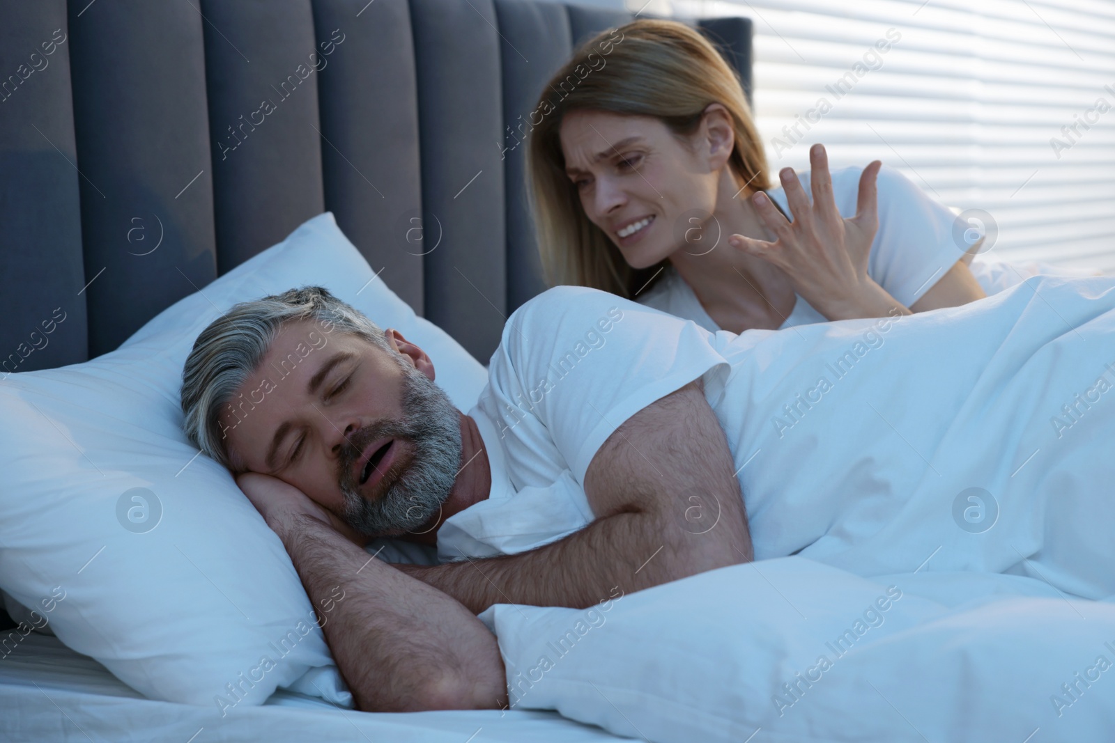 Photo of Irritated woman near her snoring husband in bed at home