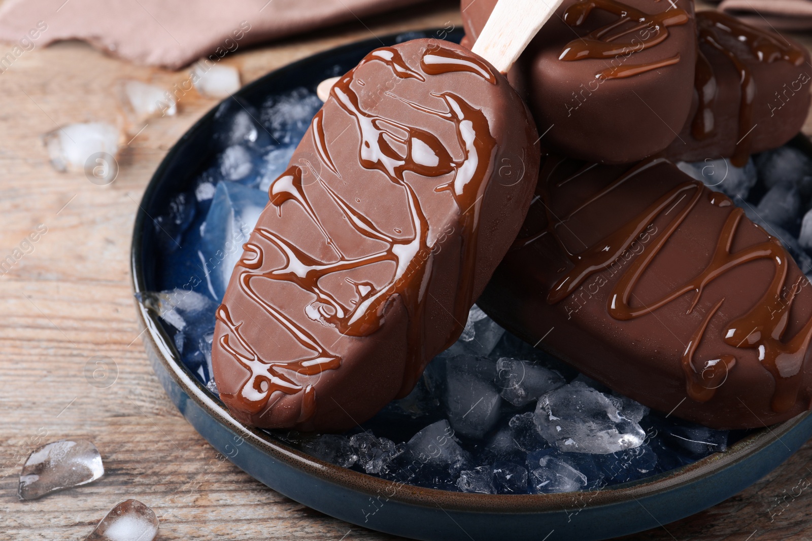 Photo of Delicious glazed ice cream bars and ice cubes on wooden table, closeup