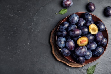 Delicious ripe plums on black table, flat lay. Space for text