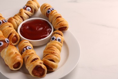Photo of Plate with tasty sausage mummies for Halloween party and ketchup on white table, closeup. Space for text