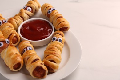 Plate with tasty sausage mummies for Halloween party and ketchup on white table, closeup. Space for text