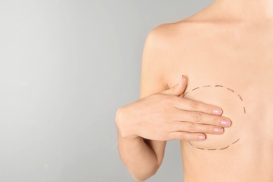 Photo of Young woman with marks on breast for cosmetic surgery operation against gray background, closeup. Space for text