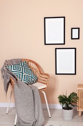 Photo of Empty frames hanging on beige wall, wicker chair and potted plant indoors