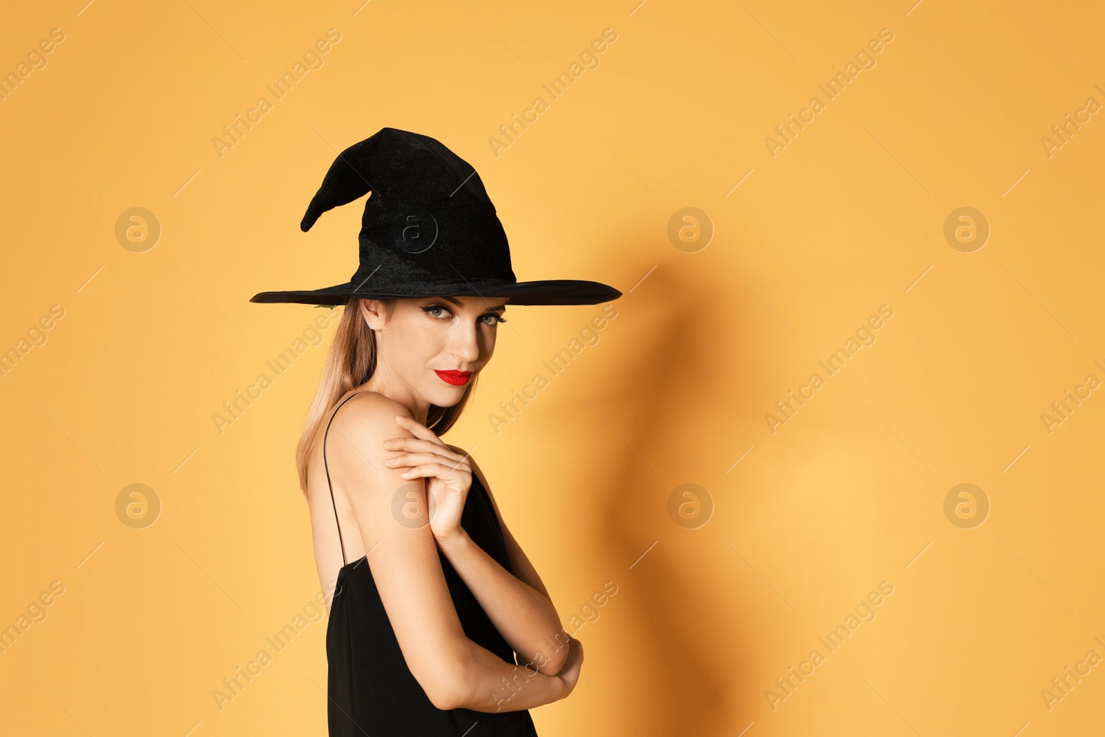 Photo of Beautiful woman wearing witch costume for Halloween party on yellow background, space for text