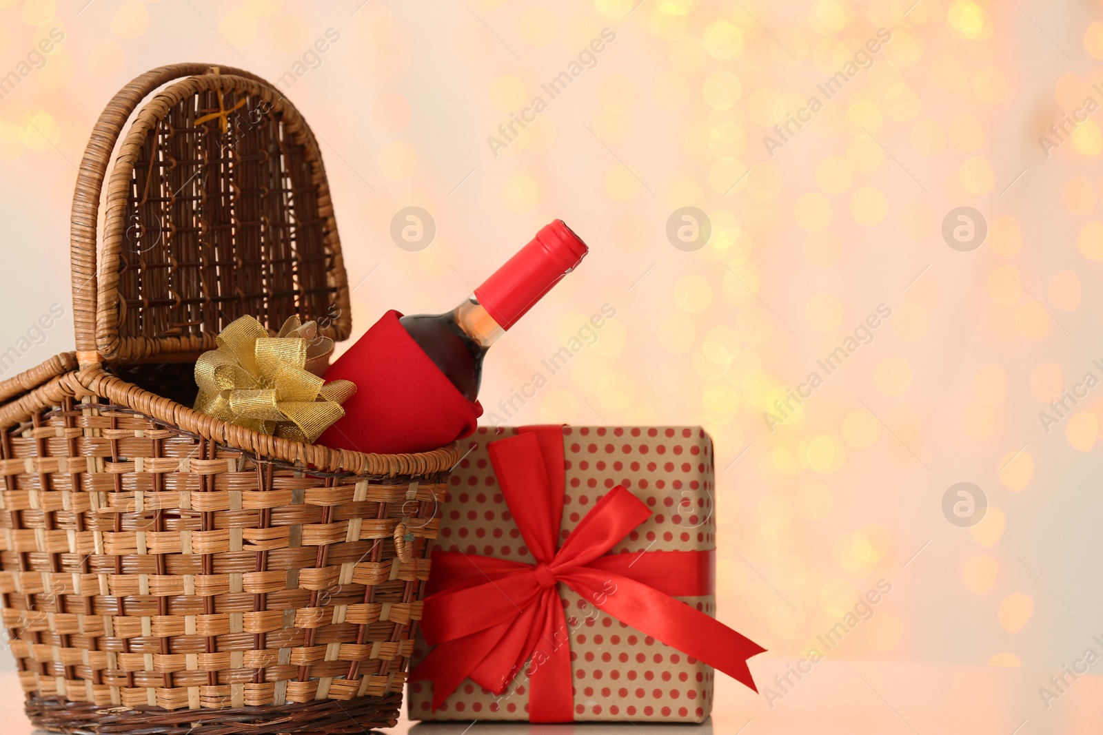 Photo of Wicker basket with bottle of wine and gift box against blurred background. Space for text