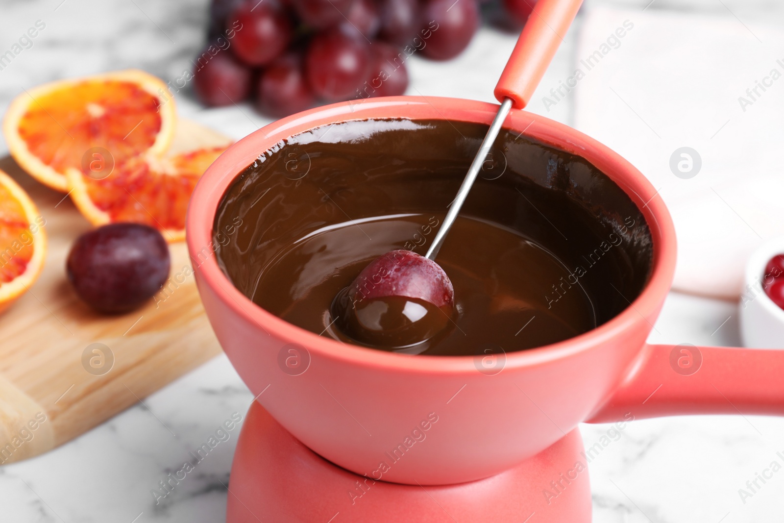 Photo of Dipping grape into pot with chocolate fondue on table, closeup