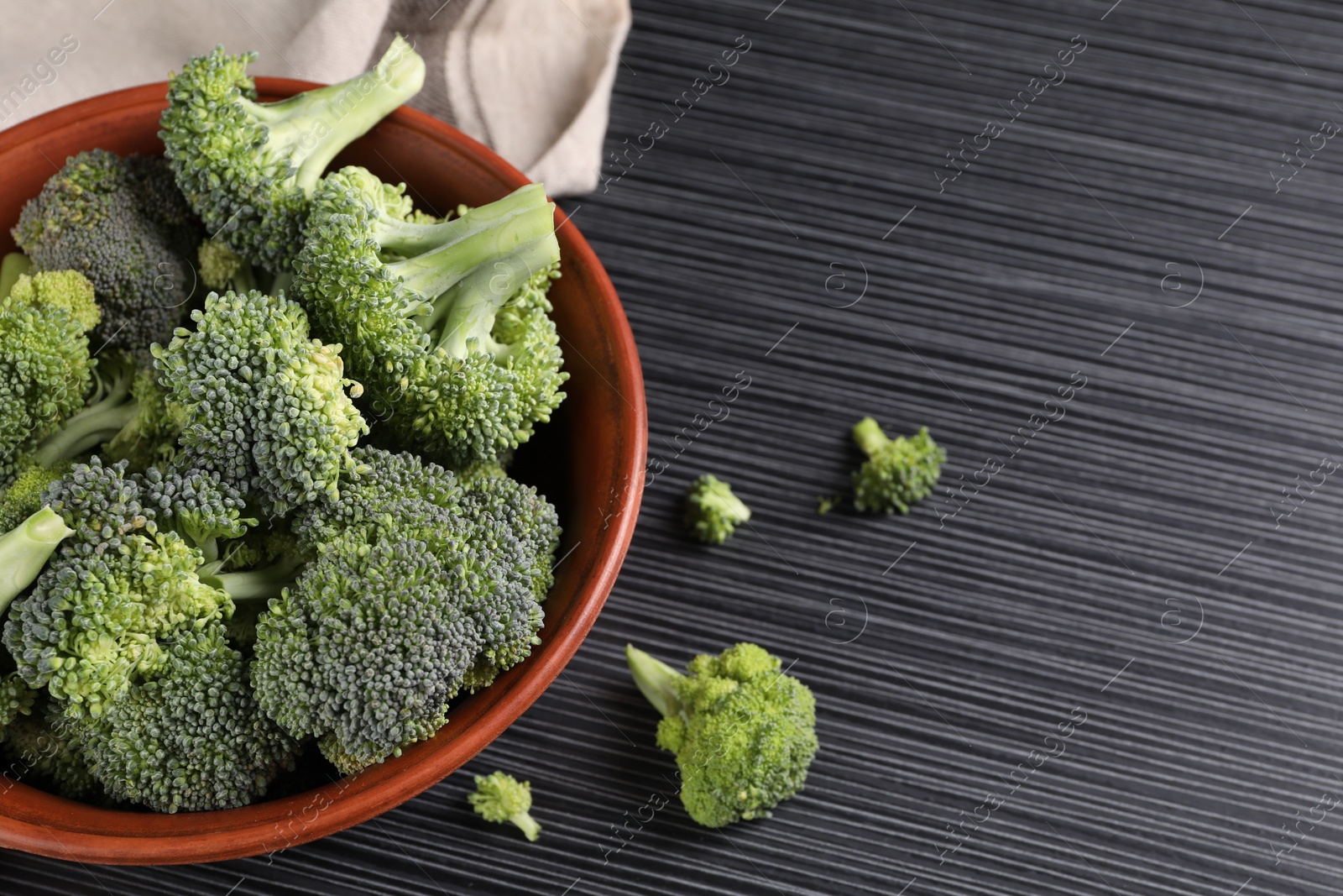 Photo of Bowl with fresh raw broccoli on black wooden table. Space for text