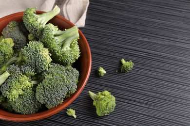 Bowl with fresh raw broccoli on black wooden table. Space for text