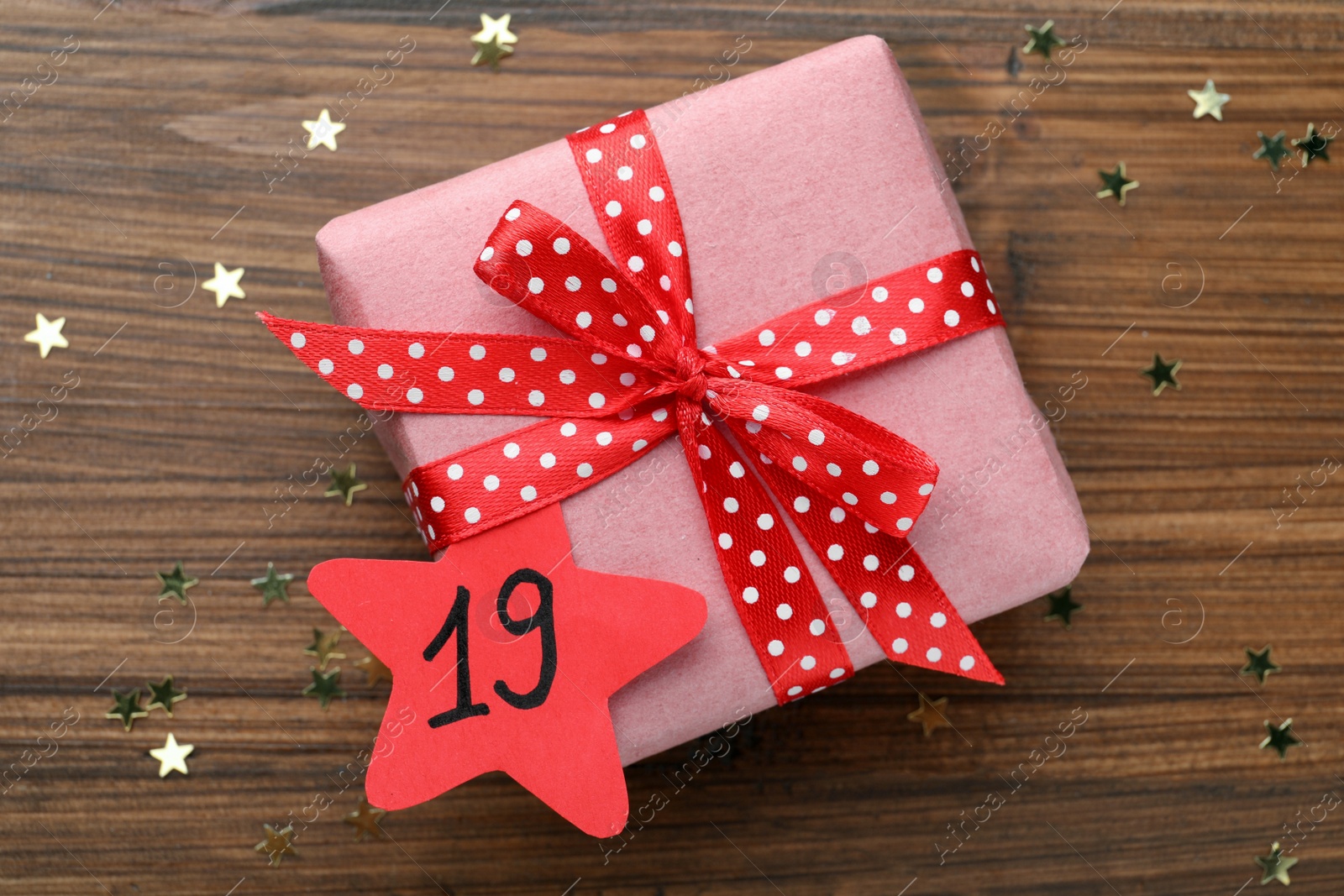 Photo of Saint Nicholas Day. Wrapped gift box with date December 19 and star shape confetti on wooden table, top view