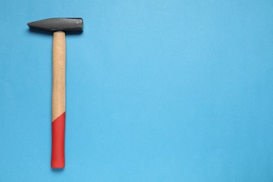 New hammer with wooden handle on light blue background, top view. Space for text