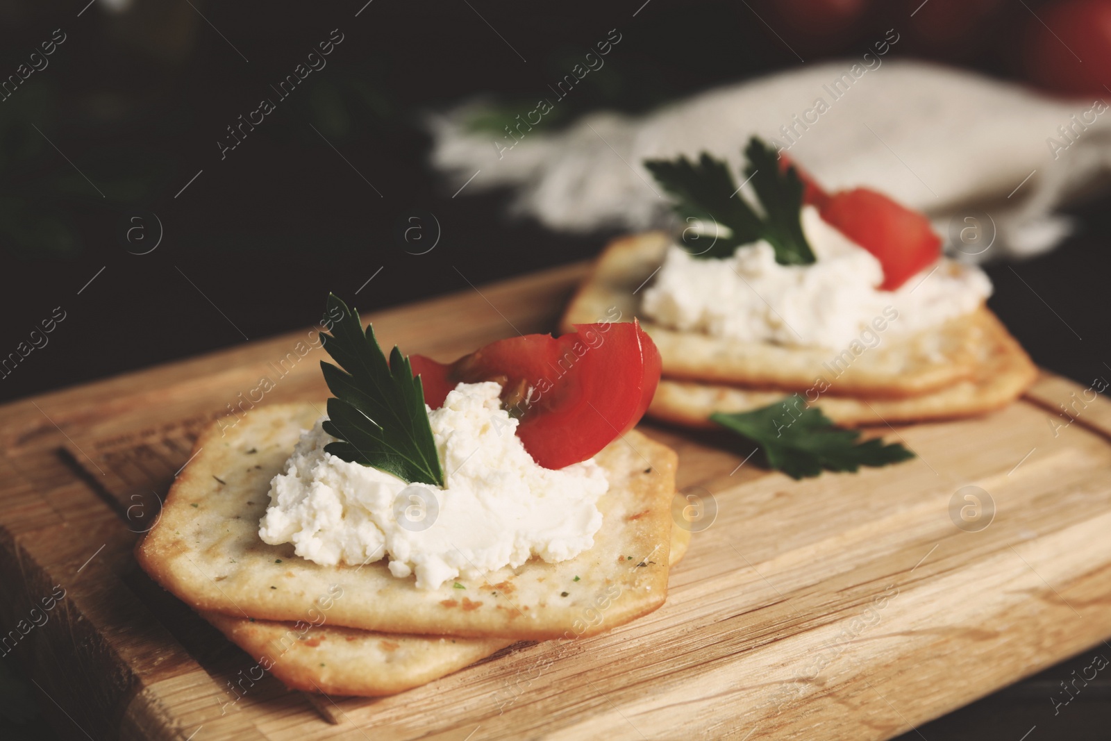 Photo of Delicious crackers with cream cheese, tomato and parsley on wooden board, closeup