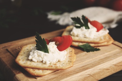 Photo of Delicious crackers with cream cheese, tomato and parsley on wooden board, closeup