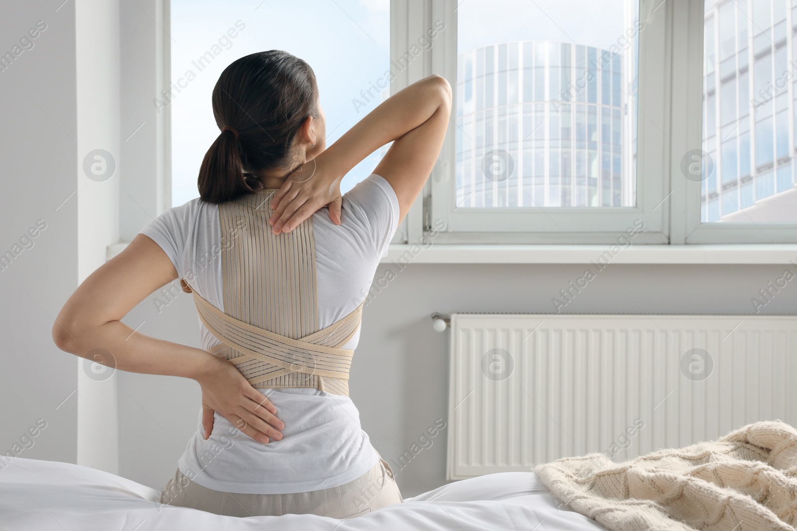 Photo of Woman with orthopedic corset sitting in bedroom, back view