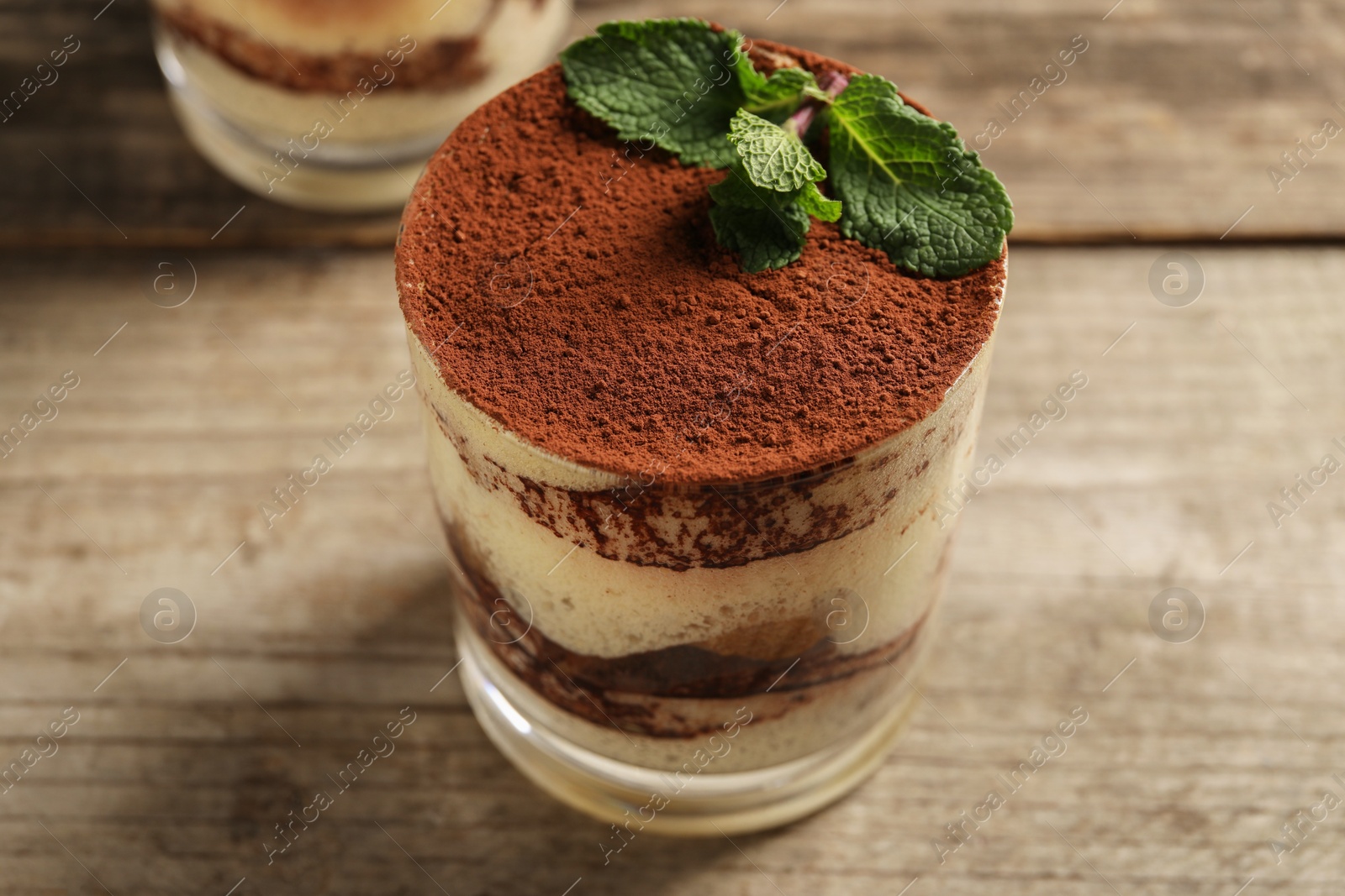 Photo of Tasty tiramisu and mint in glass on wooden table, closeup