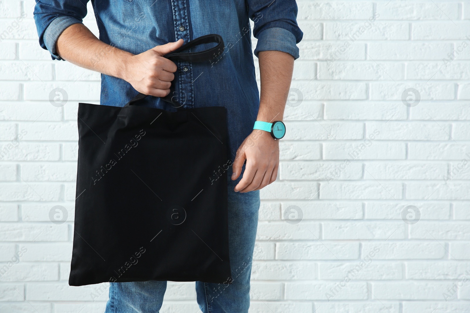 Photo of Young man holding textile bag against brick wall, closeup.  Mockup for design