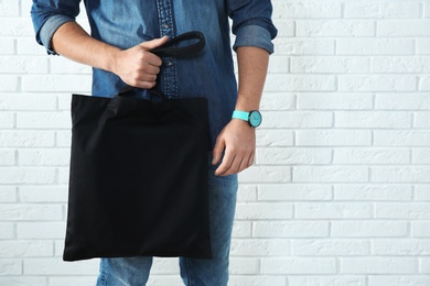 Photo of Young man holding textile bag against brick wall, closeup.  Mockup for design