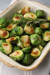 Photo of Delicious roasted Brussels sprouts and rosemary in baking dish on table, closeup