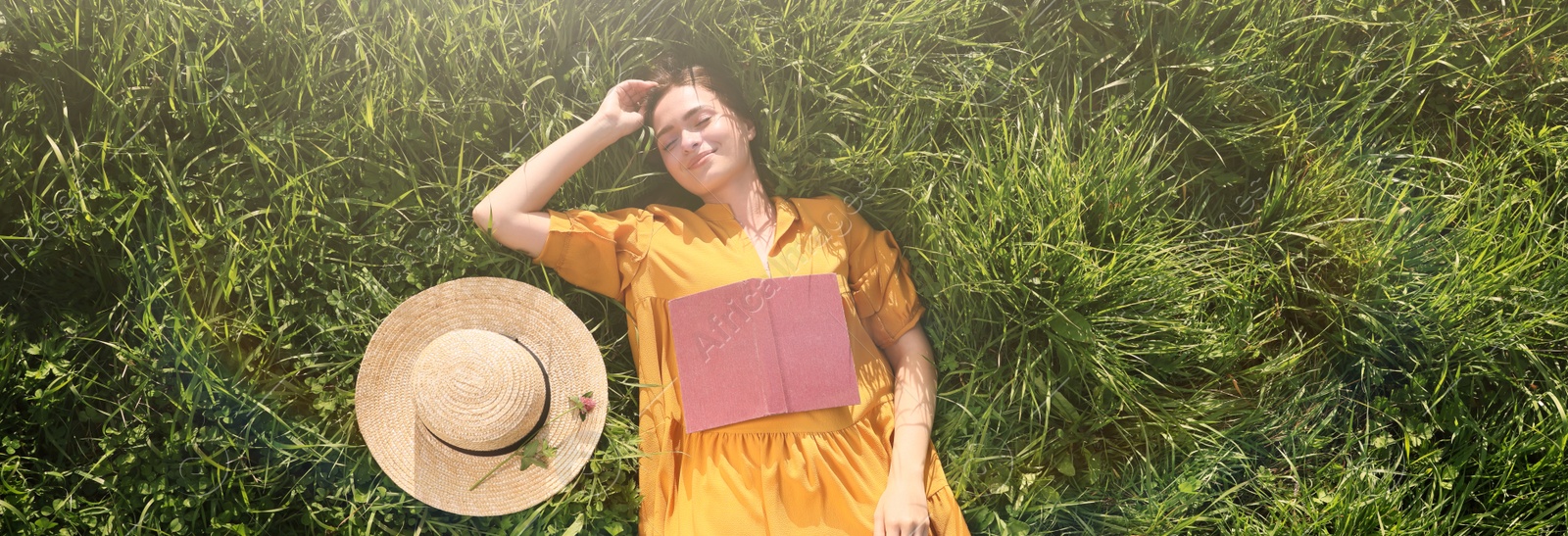 Image of Beautiful young woman with book lying on green meadow, top view. Banner design