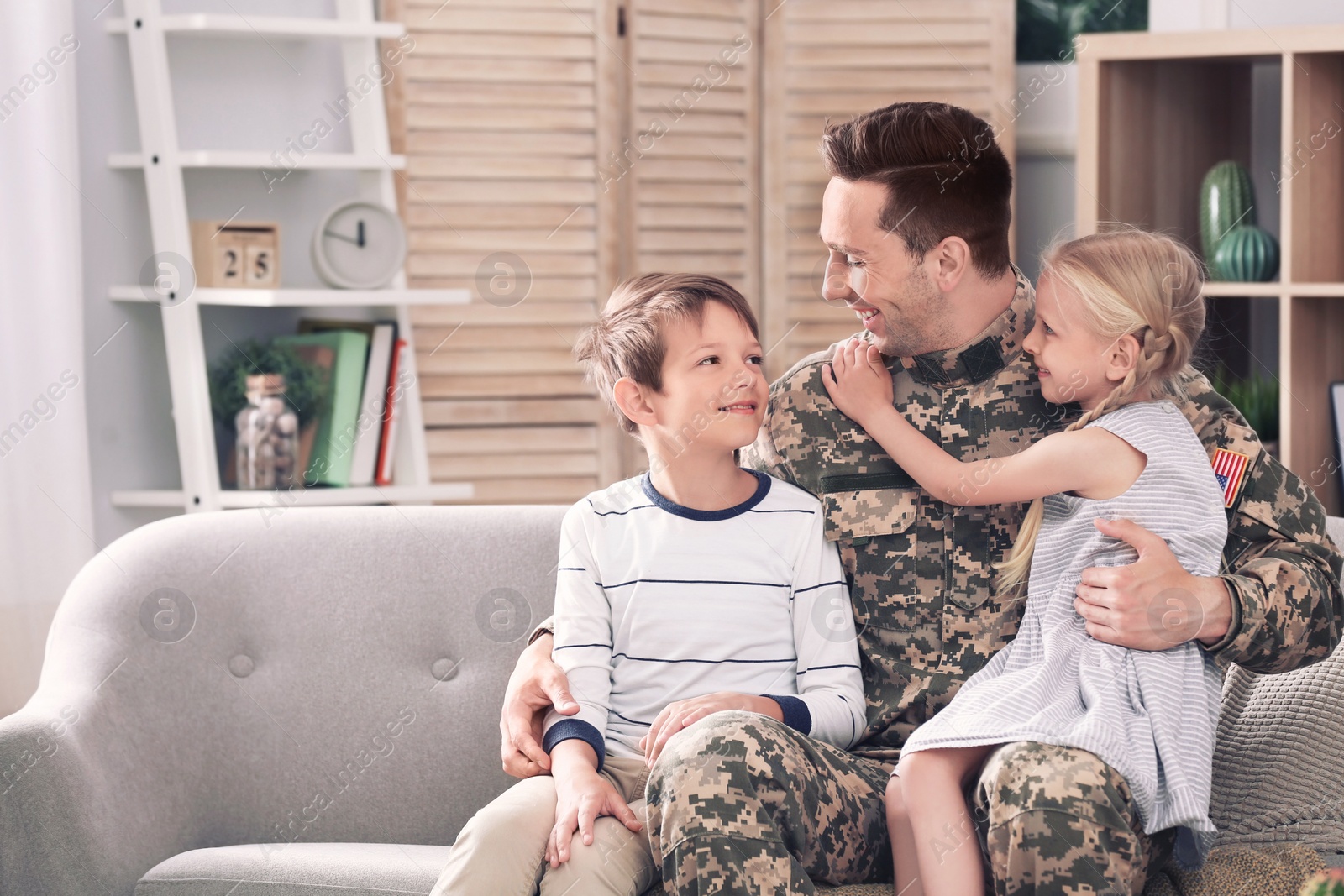 Photo of Young man in military uniform with his children on sofa at home