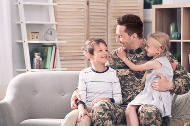 Photo of Young man in military uniform with his children on sofa at home