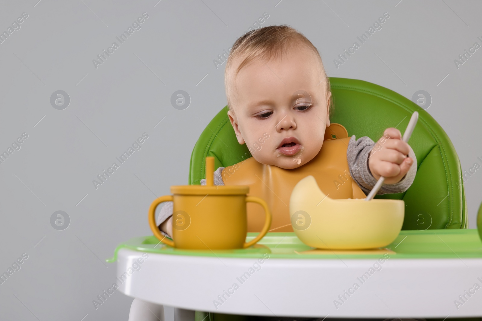 Photo of Cute little baby eating healthy food in high chair on gray background, space for text