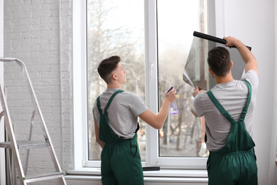 Professional workers tinting window with foil indoors